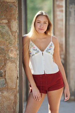 Beautiful young Latina woman posing in desert wearing thin strapped blouse and red shorts - in doorway of building ruins