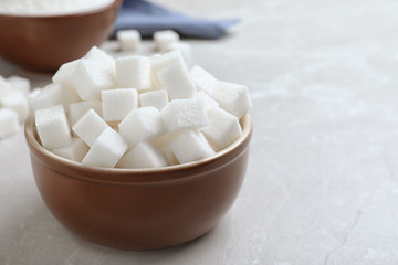 Fototapeta na wymiar Refined sugar cubes in bowl on light grey table