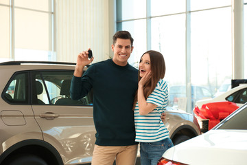 Happy couple with car key in modern auto dealership