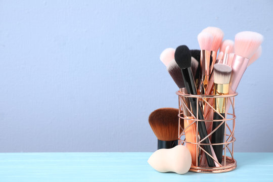 Set of professional makeup brushes in holder on blue wooden table. Space for text