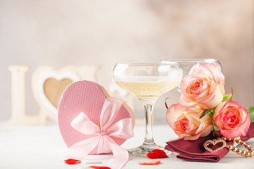 Champagne glasses, a bouquet of roses and a gift on a bright background. Romantic celebration of Valentine's day