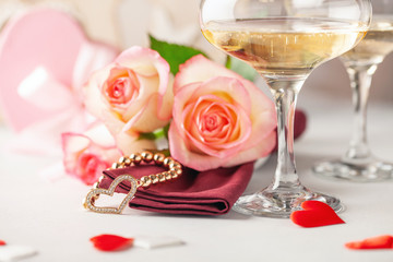 Champagne glasses, a bouquet of roses and a gift on a bright background. Romantic celebration of Valentine's day