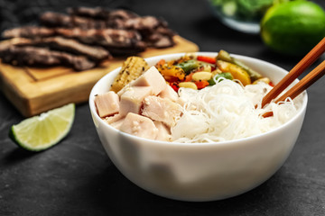 Tasty cooked rice noodles with chicken and vegetables on black table, closeup