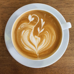 Top view of a mug of latte art coffee on timber background.