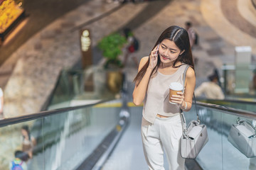 Young Asian woman passenger using smart mobile phone and walking up escalator in department store when traveling in city,japanese,chinese,Korean lifestyle and daily life,commuter and transportation