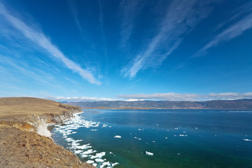 Fototapeta na wymiar Lake Baikal on a sunny May day. Beautiful spring landscape with white ice floes near the shore of the island of Olkhon and unusual layered clouds in the blue sky. Natural background