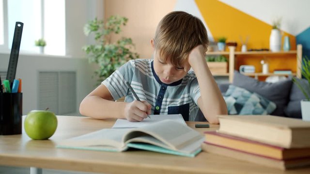 Portrait of smart kid in casual clothing doing homework at home studying writing reading sitting at desk alone. Education, childhood and literacy concept.