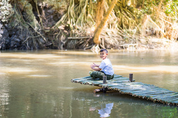 Kid boy sit on the Bamboo bridge beside the lake