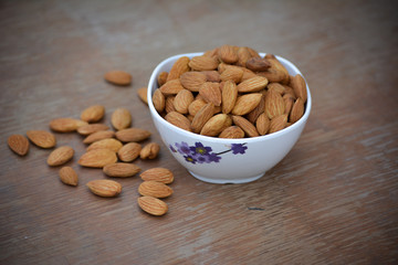 Almonds in white bowl on wooden background
