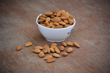 Almonds in white bowl on wooden background