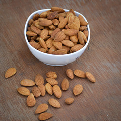Almonds in white bowl on wooden background