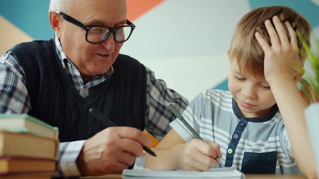 Cheerful people old man and small boy studying at home writing doing school homework sitting at desk together. Family, lifestyle and education concept.