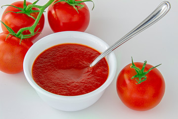 Fresh tomatoes sauce on a white plate with a spoon and  tomato berries on the side.