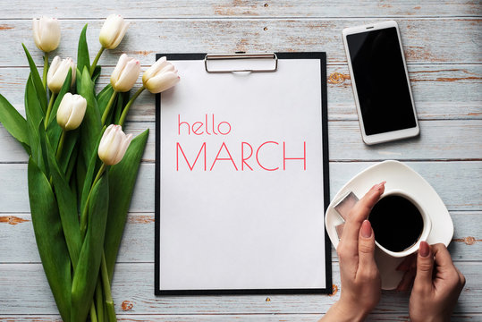 Greeting card with the inscription Hello March. Bouquet of white Tulip flowers with a Cup of coffee and a smartphone