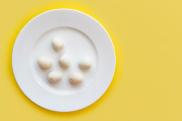 Set of peeled organic small boiled quail eggs on white plate on yellow background. Top view, copy space. Healthy protein fresh natural food. Natural gourmet meal. Little bird eggs.