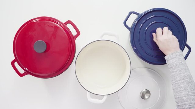Flat lay. Red, white and blue enameled cast iron covered round dutch ovens on a white background.