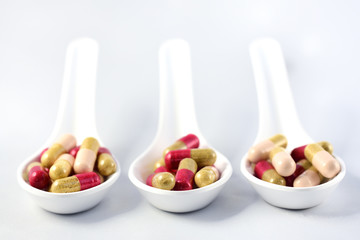 Three large white spoons filled with capsules stand against a white background in medicine for taking medication