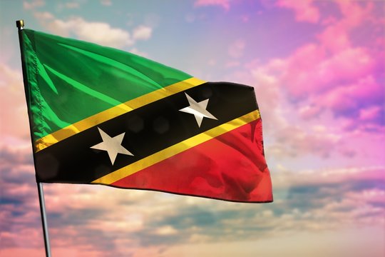 Fluttering Saint Kitts and Nevis flag on colorful cloudy sky background. Prosperity concept.