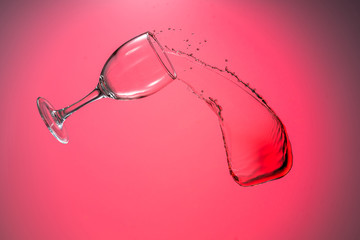 wine glass falls with a big splash of red wine flow on a red background
