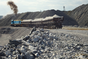 Diesel locomotive is pushing dump-car filled with rubble stone in the background of a quarry for limestone mining.