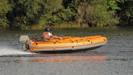 Orange Inflatable outboard motor boat with racer in lifejacket and helmet fast planing floats on...