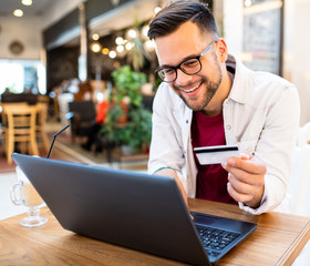 A man in a cafe with a laptop and a credit card, shopping online.