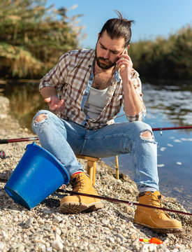 Concerned Fisherman Talking On Mobile Phone By The River