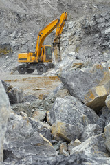 Wheel excavator with a hydraulic hammer working in a quarry, with huge fragments of rock in the...