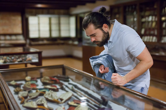Attentive Adult Man Exploring Artworks In Glass Case In Museum