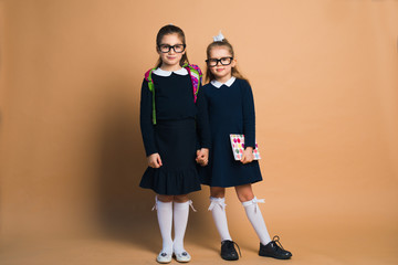 two girls in school uniform posing with copybook and backpack on color background
