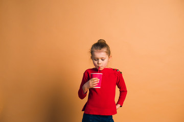 happy child wearing fashion casual jeans, sweater and sunglasses posing with cup of coffee on color background