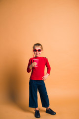 Fototapeta na wymiar happy child wearing fashion casual jeans, sweater and sunglasses posing with cup of coffee on color background