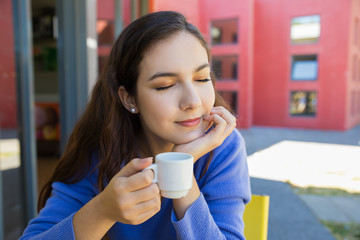Beautiful young woman with closed eyes holding cup of coffee. Closeup shot of young woman enjoying taste of delicious coffee. Coffee taste concept