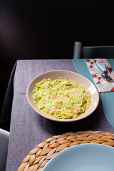 Green guacamole sauce on a plate served on a dining table on a black background