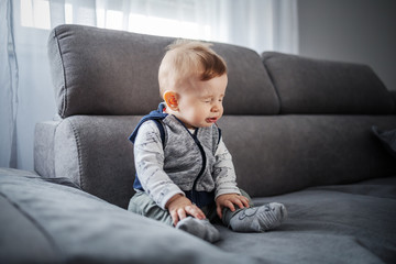 Adorable little boy sitting on couch in living room and sneezing.
