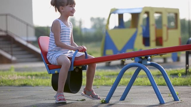 Cute child girl playing outside on a see-saw swing at preschool playground.