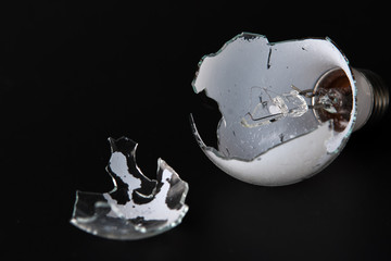 Broken light bulb isolated on black background with shattered piece of lightbulb.