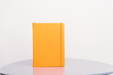 Orange book, agenda or planner standing on a grey surface and white background. Book template.
