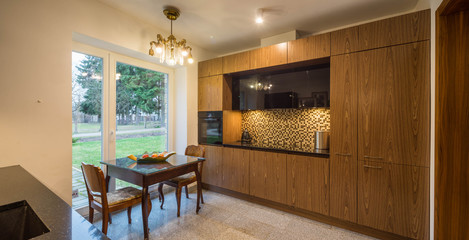 Interior of modern kitchen in private house. Wooden kitchen set. Home appliances. Table by the window.