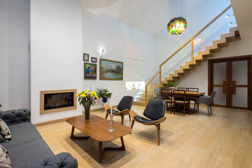 Light interior of room in private house. Entrance door. Staircase. Fireplace. Tables and chairs.