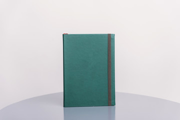 Dark green book, agenda or planner standing on a grey surface and white background. Book template.