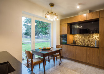 Interior of modern kitchen in private house. Wooden kitchen set. Home appliances. Table by the window.