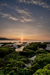 Fototapeta premium Sunrise over a beach with coral reefs covered by green moss in Sawarna, Banten, Indonesia