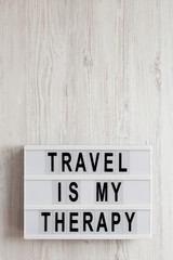 'Travel is my therapy' words on a lightbox on a white wooden background, top view. Overhead, from above, flat lay. Copy space.