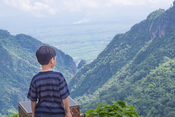 Naklejka premium Back view of boy kid standing and looking to the beautiful mountains view. Feeling happiness and freedom. Space for text