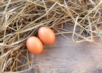 Close-up 2 eggs near straw on wooden background.
