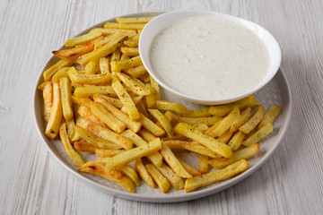 Homemade Crispy Ranch Fries on a gray plate on a white wooden background, side view. Close-up.