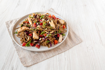 Homemade Spicy Chicken Soba Noodle Salad on a gray plate on a white wooden background, side view. Copy space.