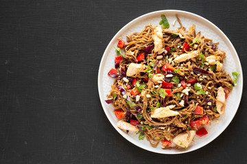 Homemade Spicy Chicken Soba Noodle Salad on a gray plate on a black background, top view. Flat lay, overhead, from above. Copy space.
