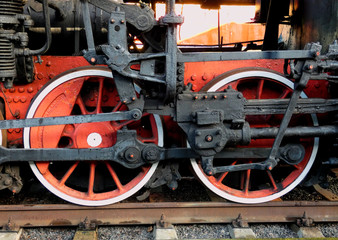 Fototapeta premium Old steam engine locomotive wheels and other parts, close-up view. Black and red iron details of vintage train. Industrial retro background.